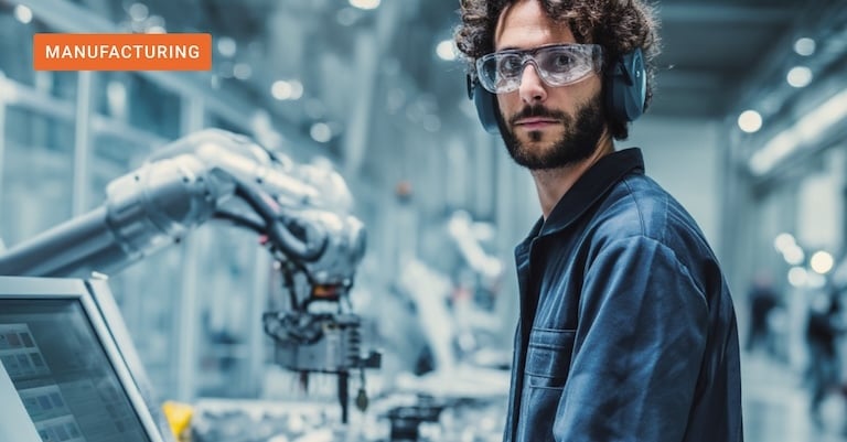  A technician with safety gear standing next to a robotic arm and digital interface, representing agentic AI in manufacturing and the shift to intelligent machine partners.