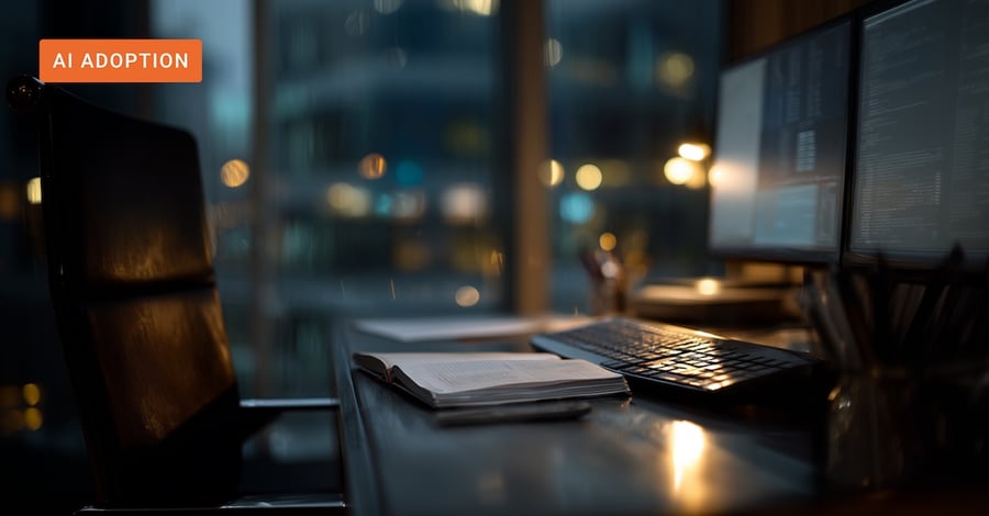 Empty office chair at a workstation with monitors showing code, open notebook on the desk, city lights visible at night.