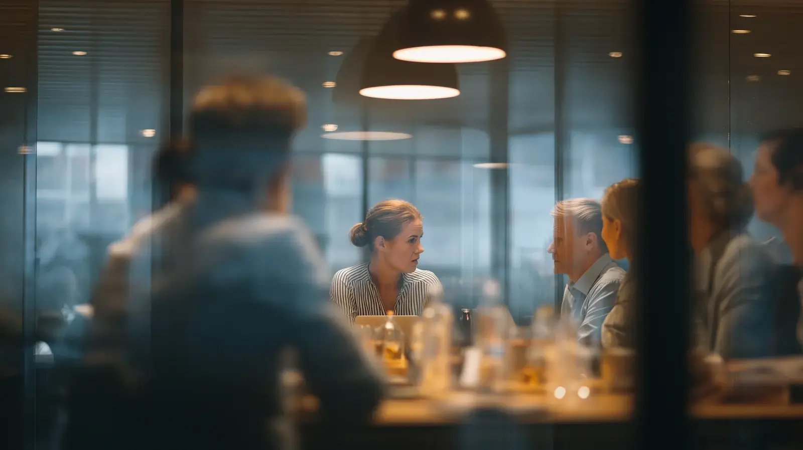 A team meeting in a glass meeting room under warm pendant lights